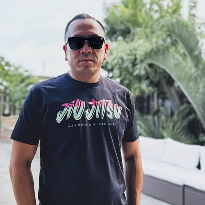 Wearing the "City Connect - Black" T-shirt, a person stands outdoors with sunglasses, embodying the camaraderie of the Jiu Jitsu community, surrounded by greenery and outdoor furniture.