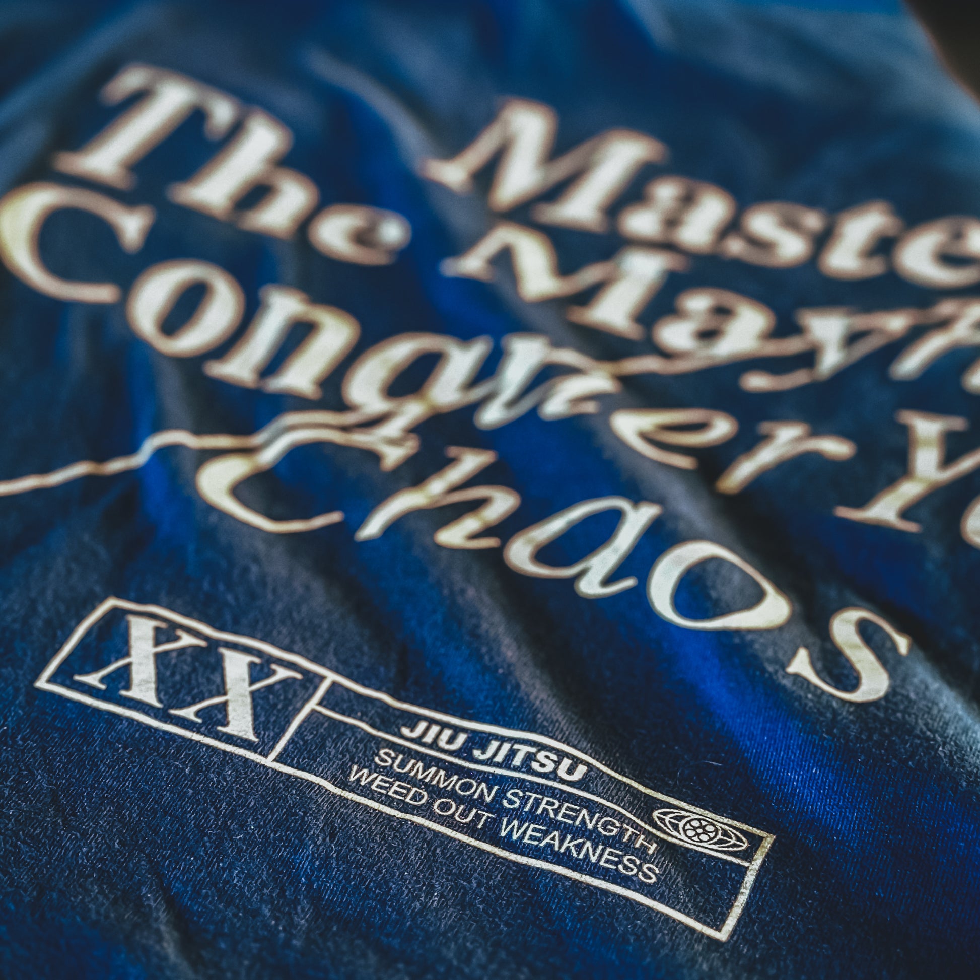 A royal blue T-shirt showcasing the phrase "Master The Mayhem, Conquer Your Chaos" along with a stylish "XX Jiu Jitsu, Summon Strength, Weed Out Weakness" logo.