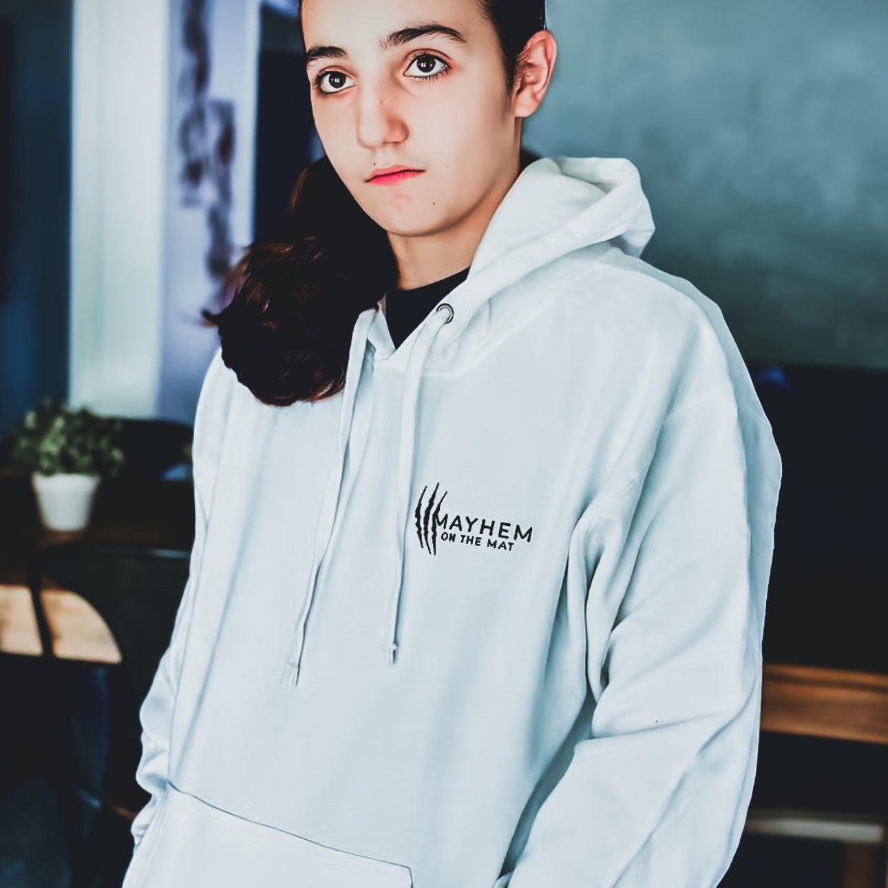 A person wearing the "Earn Your Stripes - White" hoodie, standing indoors with the "Mayhem on the Mat" logo, truly embodies the spirit of warriors. The design is sleek and captivating.