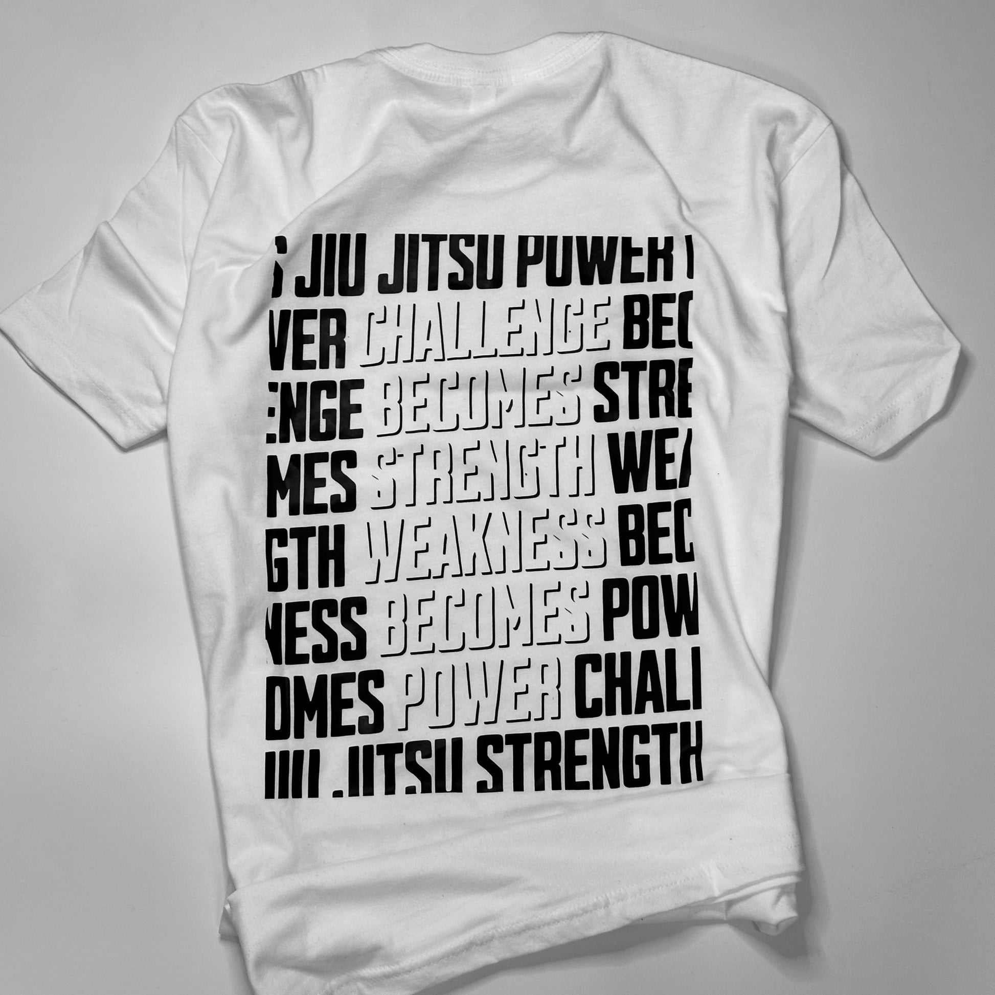 White T-shirt from the "Strength & Power - White" collection, featuring bold black text: "Jiu jitsu power, challenge becomes strength, weakness becomes empowerment, jiu jitsu strength.