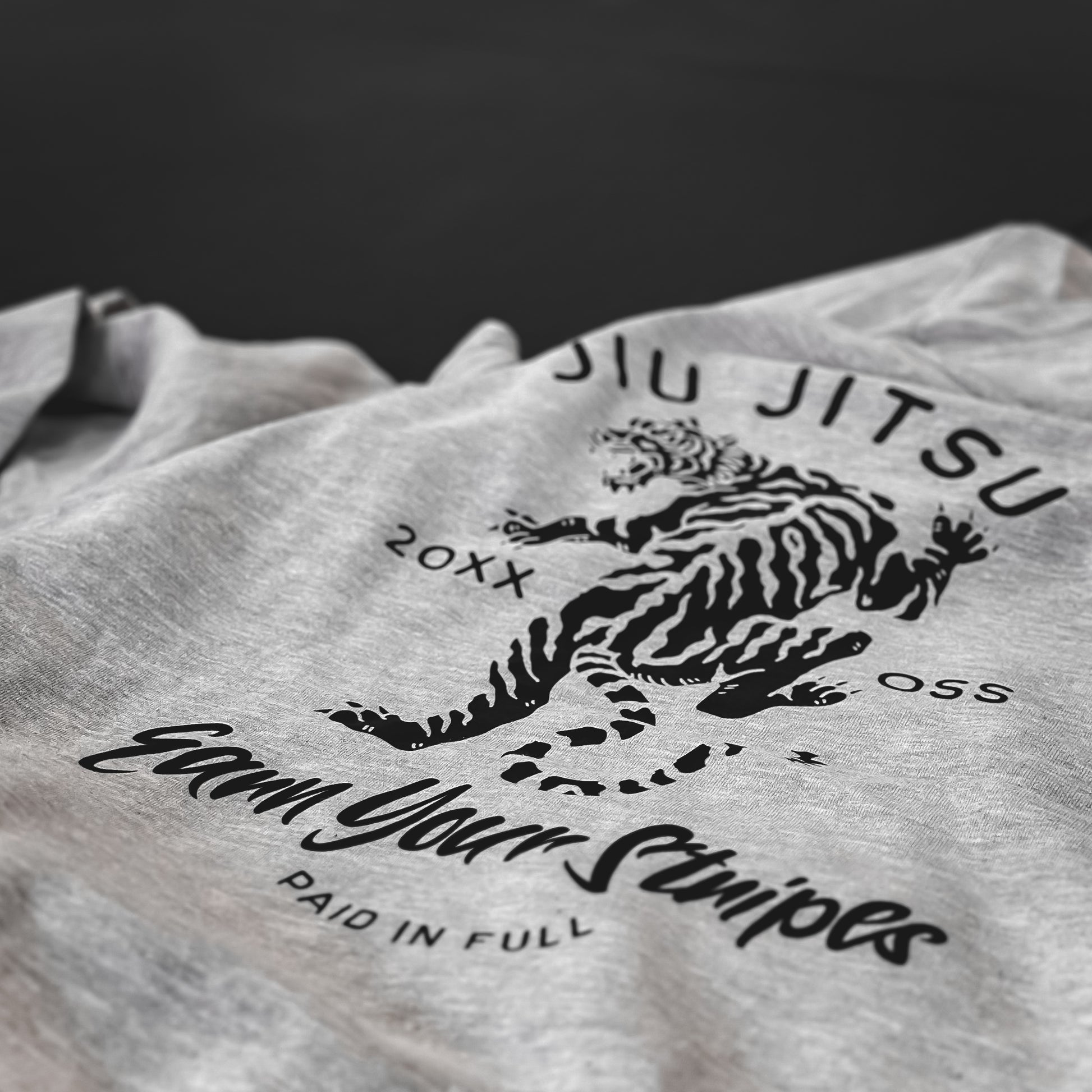 Heather Grey T-shirt featuring a bold black tiger graphic and Jiu Jitsu-themed text: "Earn Your Stripes, Paid in Full." This striking design honors the unwavering dedication of warriors striving for excellence.